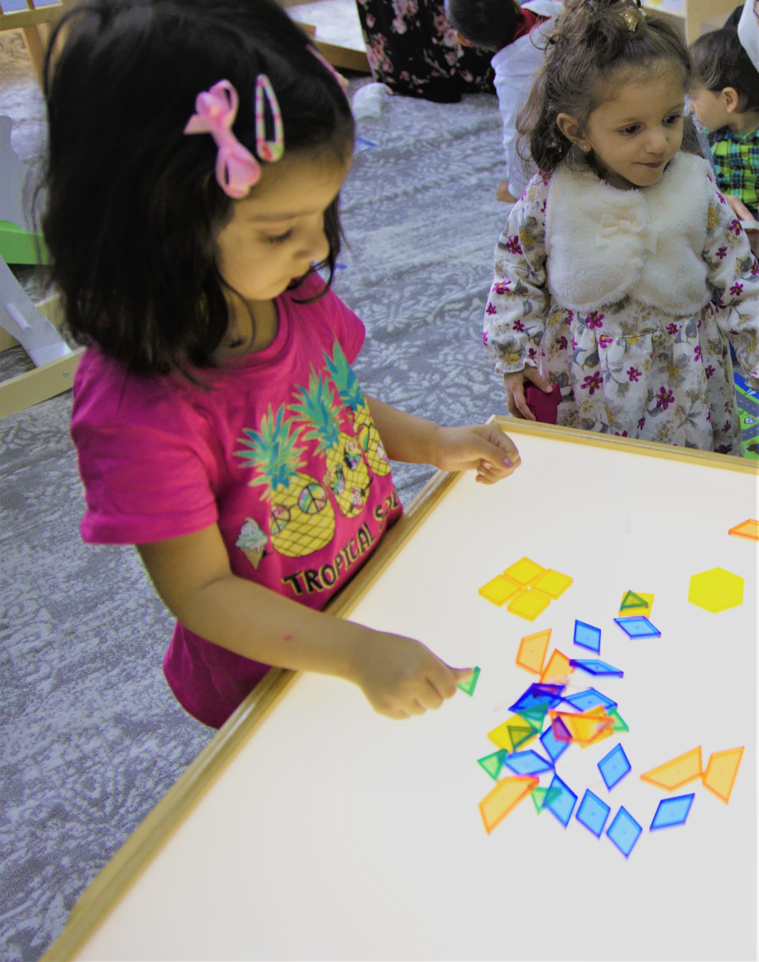 Children arranging colorful geometric shapes on a light table