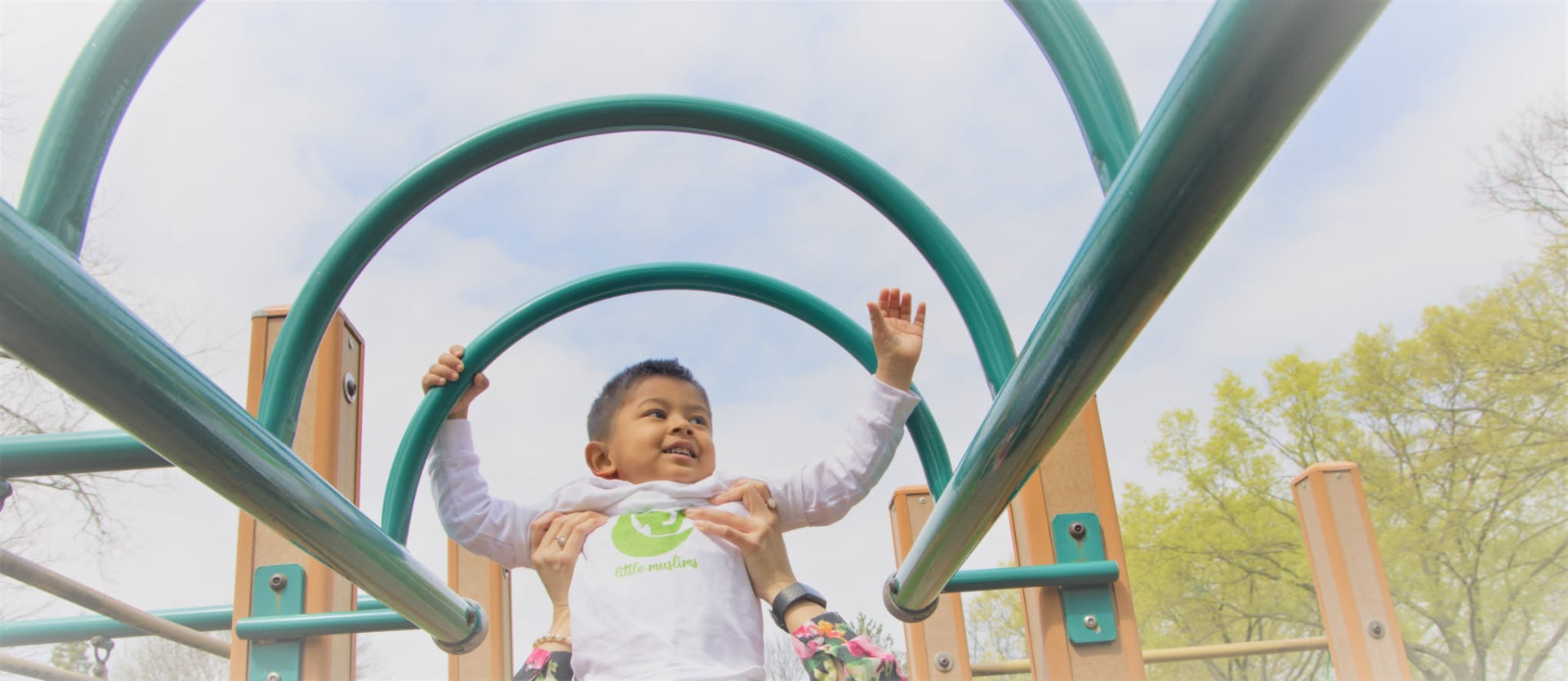 Child climbing on playground monkey bars with a teacher