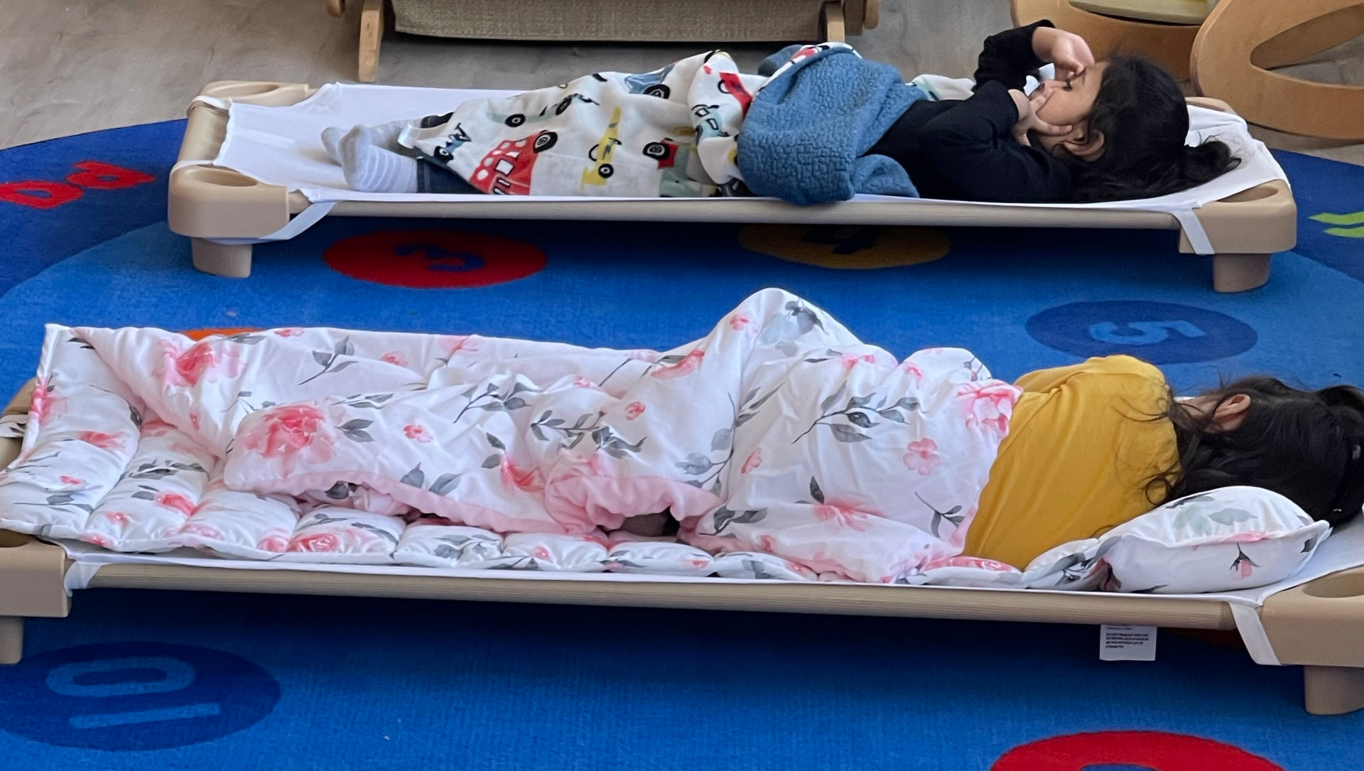 Two children resting on cots with cozy blankets during nap time