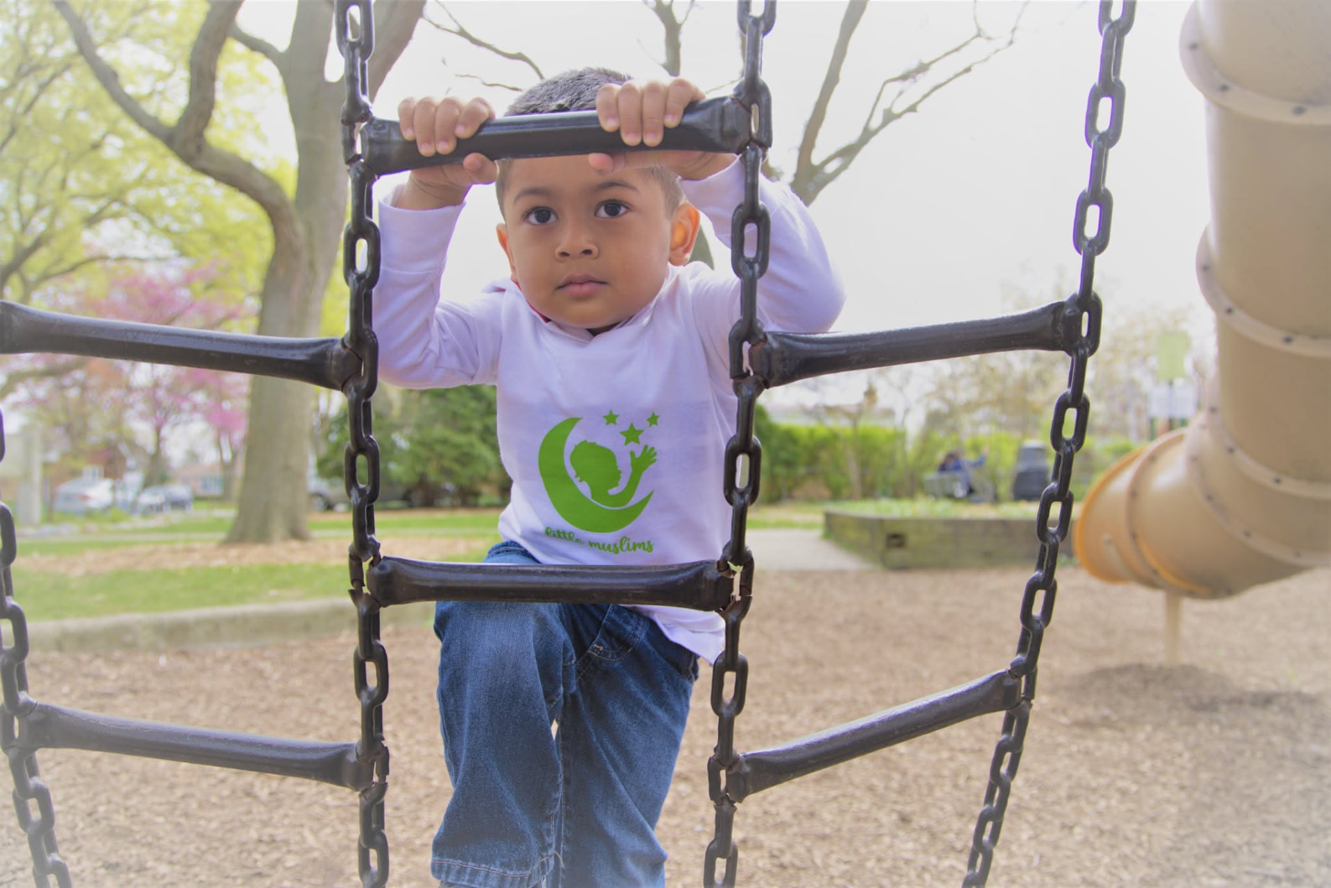 A child smiling while climbing on the Little Muslims playground